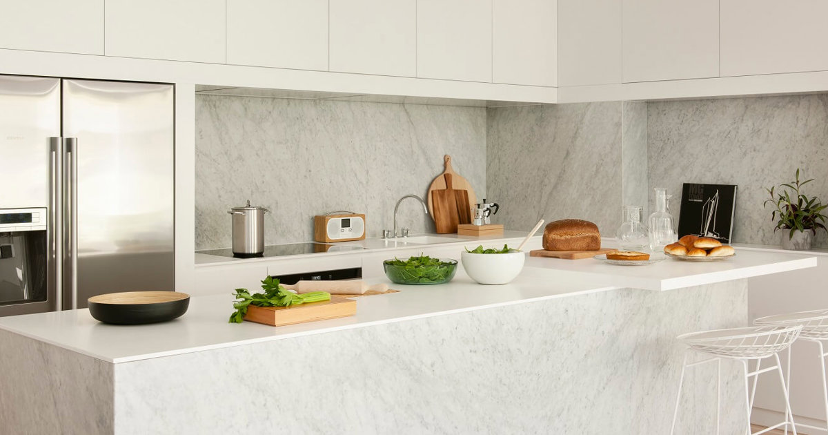 Una cocina con un mueble de cocina verde con tiradores dorados y una  encimera de mármol blanco.